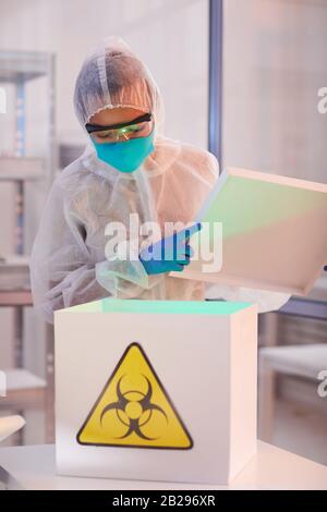 Girovita ritratto di scienziato maschile indossando biohazard scatola di apertura con cartello di pericolo mentre si lavora su ricerca in bio laboratorio, copia spazio Foto Stock