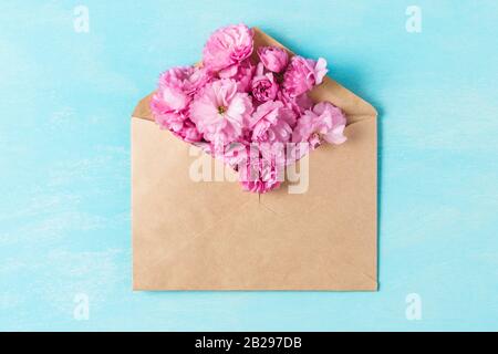 Layout creativo realizzato con fiori rosa di ciliegio in busta su sfondo blu. Appartamento. Vista dall'alto. Composizione per matrimoni o donne. Primavera co Foto Stock
