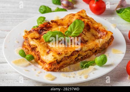 Lasagne a base di carne con basilico fresco e parmigiano in un piatto su un tavolo di legno bianco. Primo piano. Cibo italiano. Foto Stock