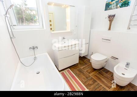 Bagno bianco in stile minimalista. Piastrelle bianche luminose, bagno, wc, lavandino, piastrelle beige sul pavimento. Elegante, alla moda, minimalista. Foto Stock