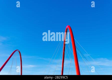 Parzialmente bella struttura ad arco rosso curvato e cavo di sospensione ponte con sfondo di cielo blu chiaro. Foto Stock