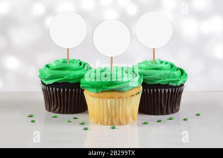 Tre deliziosi cupcake verdi smerigliati riposano su uno sfondo di marmo bianco circondato da verdi spruzzi. Giornata di San Patrizio o una squadra di sport Cuca Foto Stock