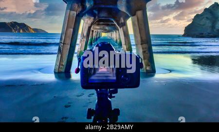 Usando la mia seconda macchina fotografica per catturare una lunga esposizione su un treppiede sotto lo storico molo di legno a Tolaga Bay all'alba Foto Stock