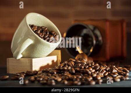 Chicco di caffè nella tazza bianca e il macinino da caffè sul tavolo di legno. Concetto colazione o tempo di caffè la mattina. Foto Stock