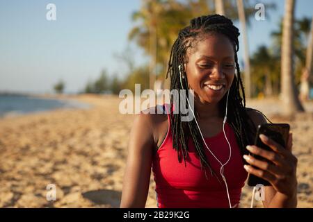 Jogger femminile piuttosto positivo fare una videochiamata al suo allenatore dopo l'allenamento Foto Stock