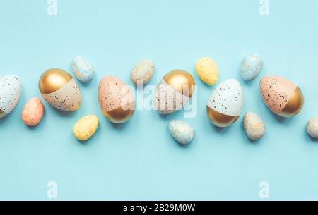 Vista dall'alto delle uova di Pasqua colorate con vernice dorata e colori diversi. Sfondo blu. Spazio di copia. Foto Stock