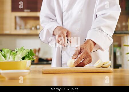 Immagine ritagliata del cuoco che taglia le uova bollite su tavola di legno al tavolo della cucina Foto Stock