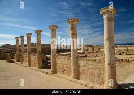 Antiche colonne con capitelli ionici contro il cielo blu con sfondo nuvole. Piccolo mare blu è visibile al centro. Rovine della città di Salamis, Northen Cyp Foto Stock