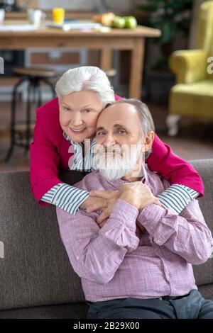 Bella donna dai capelli grigi che abbraccia suo marito e sorride Foto Stock