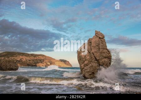 Illuminato con sole serale Aphrodite Rock (Petra tou Romiou o Rocca del Greco - Cipro) nel mare infuriato. Cielo blu con nuvole sullo sfondo. Foto Stock