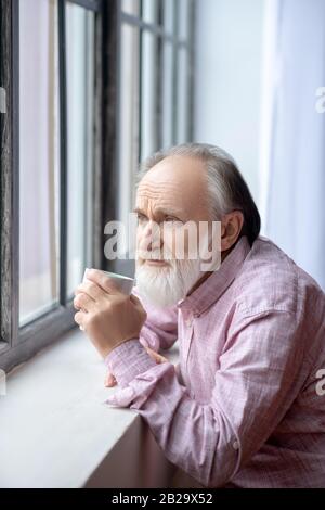 In piedi con capelli grigi e bearded vicino alla finestra, sono molto premurosi Foto Stock