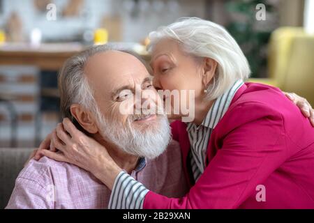 Donna anziana dai capelli verdi che bacia il suo felice marito barbuto su una guancia Foto Stock