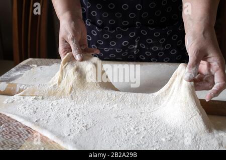 La donna anziana allunga l'impasto durante l'estrazione della pasta nella sua cucina di casa. Pasta fatta in casa o produzione di pasta da nonna. Primo piano, focu selettivo Foto Stock