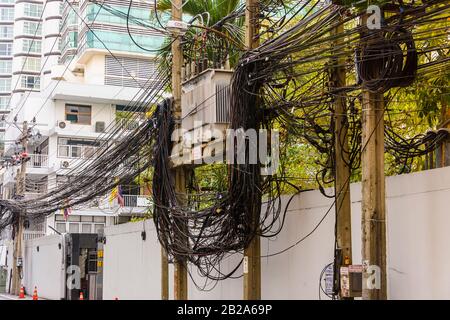 Cavi elettrici disordinati e disordinati che pendono da un polo elettrico in Thailandia Foto Stock