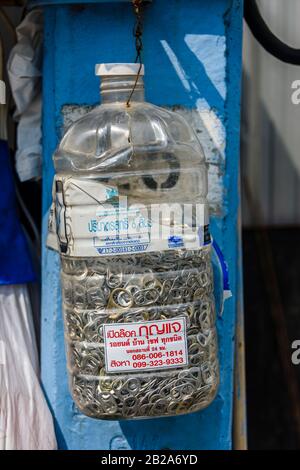 Bottiglia d'acqua in plastica contenente una raccolta di bevande può anelli tira, con un adesivo che fa pubblicità a un fabbro, Bangkok, Thailandia. Foto Stock