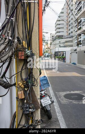 Cavi elettrici disordinati e disordinati che pendono da un polo elettrico in Thailandia Foto Stock