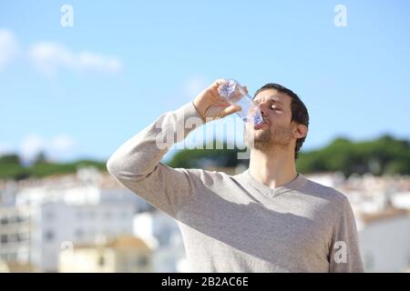 Uomo bere acqua in bottiglia in piedi in una città una giornata di sole Foto Stock