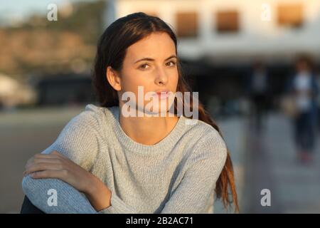 Ragazza adolescente seria che guarda la fotocamera sfidante al tramonto seduto in una città Foto Stock