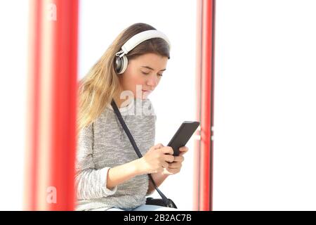 Ragazza adolescente seria che ascolta la musica che indossa le cuffie senza fili e che usa lo smartphone in una fermata dell'autobus Foto Stock