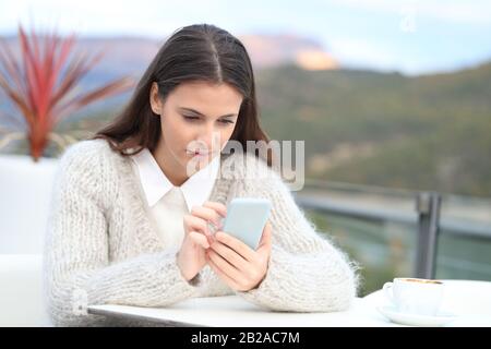 Ritratto di una ragazza adolescente che guarda il suo telefono su una terrazza in inverno con vista lago Foto Stock