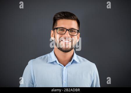 Bell'uomo che si erge su sfondo grigio scuro e che guarda sulla fotocamera. Ritratto concetto uomo. Foto Stock