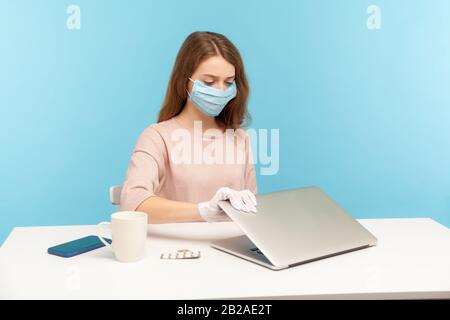 Donna dipendente che indossa maschera facciale e guanti igienici, chiusura del lavoro di finitura del laptop, quarantena e prevenzione di infezioni pericolose del coronavirus, c Foto Stock
