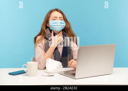 Ragazza ammalata in maschera igienica del viso seduta alla scrivania con laptop, tenendo dolore al collo dolore gola, mal di lance donna freelance con influenza che lavora da lecom Foto Stock