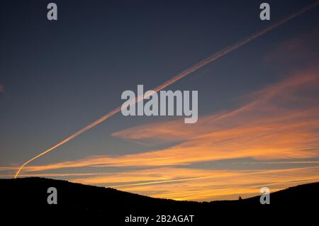 Alba arancione con contrasto arancione da un aereo a getto su una montagna silhouette Foto Stock