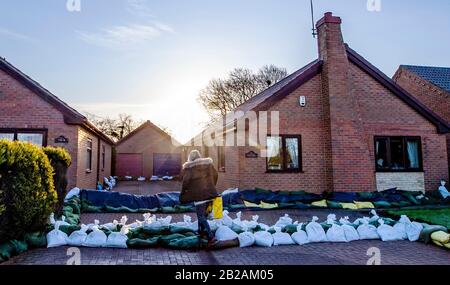 Una donna fa un passo sopra i sacchi di sabbia messi fuori per difendere una sede dalle inondazioni in East Cowick, Yorkshire. Un totale di 82 avvertimenti di alluvione sono ancora in vigore per l'Inghilterra, il Galles e la Scozia dopo gli effetti di Storm Jorge durante il fine settimana. Foto Stock