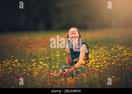 Ragazza felice seduta in un prato che raccoglie fiori selvatici, Stati Uniti Foto Stock