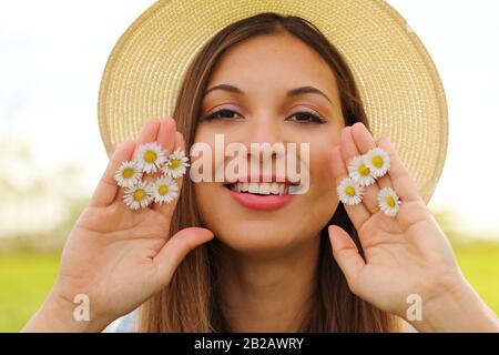 Primo piano ritratto di primavera ragazza con cappello tiene tra dita margherite fiori guardando la fotocamera Foto Stock