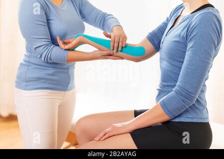 Fisioterapista femminile che applica il nastro chinesio sul braccio del paziente. Chinesiologia, terapia fisica, concetto di riabilitazione. Vista laterale dello shot ritagliato. Foto Stock