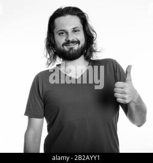 Studio shot di giovani felici uomo barbuto sorridere mentre dando pollice in alto con capelli lunghi contro uno sfondo bianco Foto Stock