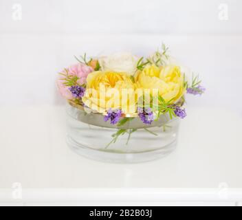 Rose gialle, rosa e bianche in un vaso di vetro su uno sfondo di una parete di legno bianco Foto Stock