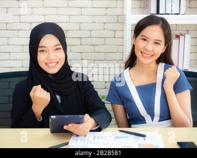 Due businesswomen musulmani stanno discutendo i guadagni dell'azienda felicemente nell'ufficio moderno. Foto Stock