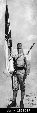 Un portabandiera africano in uniforme che appartiene al tedesco Schutztrabuppe, come Askari, in Germania Est Africa. I combattenti nativi furono reclutati dai tedeschi e da altre potenze coloniali per i loro scopi nella colonia. La maggior parte di loro non indossava una uniforme completa come l'uomo nella foto. La foto è ondulata. Foto Stock