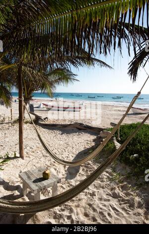 Amache su una spiaggia caraibica all'ombra delle palme. Sullo sfondo, barche da pesca su una spiaggia in Tulum Messico Foto Stock