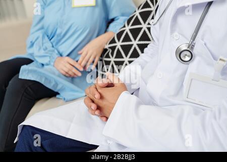 Immagine ritagliata dei lavoratori medici seduti sul divano nella sala lounge e discutere notizie e nuovi modi di trattamento Foto Stock