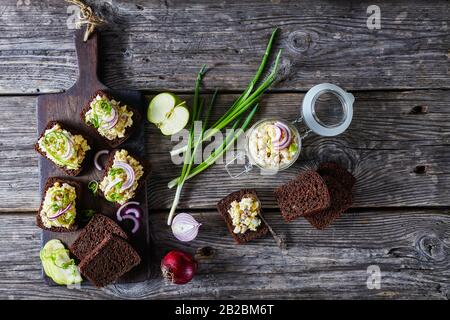 Aringa forshmak - cucina ebraica, su un pane di segale su un tagliere con ingredienti su un vecchio fondo di legno fienile, vista dall'alto, piatto lay, oriz Foto Stock