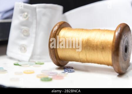 Bobina In Legno Con Filettatura Gialla Con Bottoni Assortiti E Bracciale Con Camicia Bianca Foto Stock