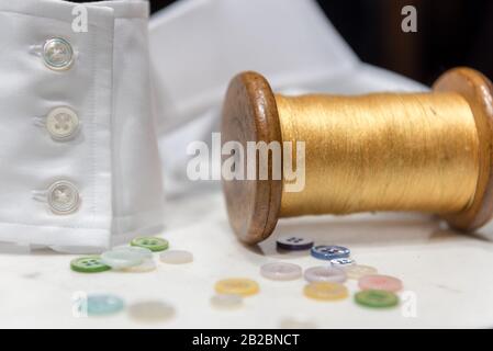 Bobina In Legno Con Filettatura Gialla Con Bottoni Assortiti E Bracciale Con Camicia Bianca Foto Stock