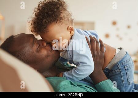 Ritratto di vista laterale di padre afro-americano che bacia il figlio del bambino mentre gioca a casa, copia lo spazio Foto Stock