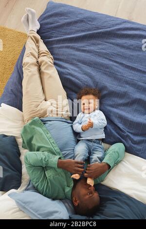 Ritratto della vista dall'alto dell'uomo afro-americano felice che gioca con il figlio cute del bambino mentre giace sul letto a casa, copia lo spazio Foto Stock