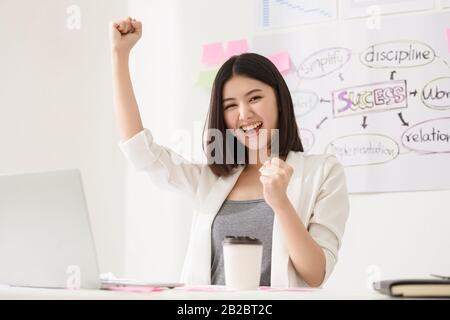 Concetto di riunione di brainstorming in team per la diversità all'avvio. Una donna di affari felice riuscita che lavora in un posto di lavoro e si sente felice e sorride ed ha alzato Foto Stock