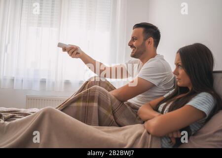 Giovane coppia sta guardando la tv nella loro camera da letto. Donna è arrabbiata. Foto Stock