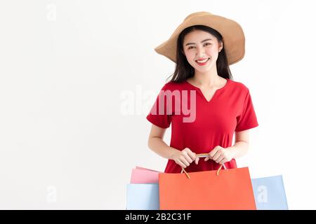 Ritratto di bella giovane donna asiatica indossando rosso lungo vestito tenendo borse di shopping isolato su sfondo bianco. Le donne fanno shopping in estate Foto Stock