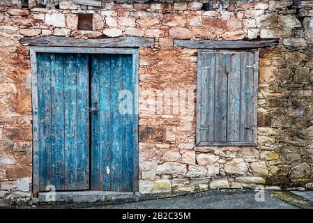 Vintage legno chiuso blu porta e finestra su un muro lapidato da una vecchia casa tradizionale in un villaggio di Cipro di Episkopi, Paphos. Foto Stock