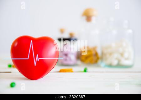 Concetto sanitario e medico. Cuore rosso su tavola di legno con set di bottiglie di medicina e sfondo pillole di medicina. Copiare lo spazio per il testo. Foto Stock