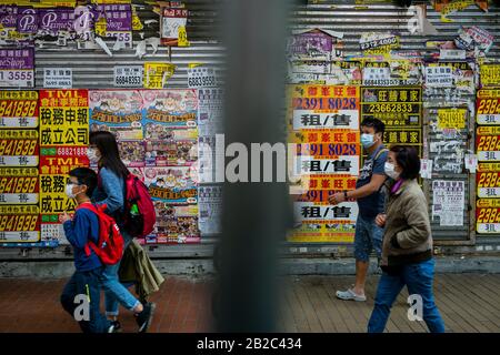 Le persone che indossano maschere protettive passano davanti a un negozio coperto di shuttered con pubblicità per lo spazio di noleggio al Causeway in mezzo Coronavirus paure a Hong Kong. Foto Stock