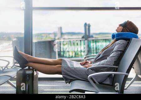Ritratto di giovane donna d'affari che dorme con il suo cuscino di testa e la mascherina dell'occhio mentre aspetta l'imbarco in aeroporto Foto Stock